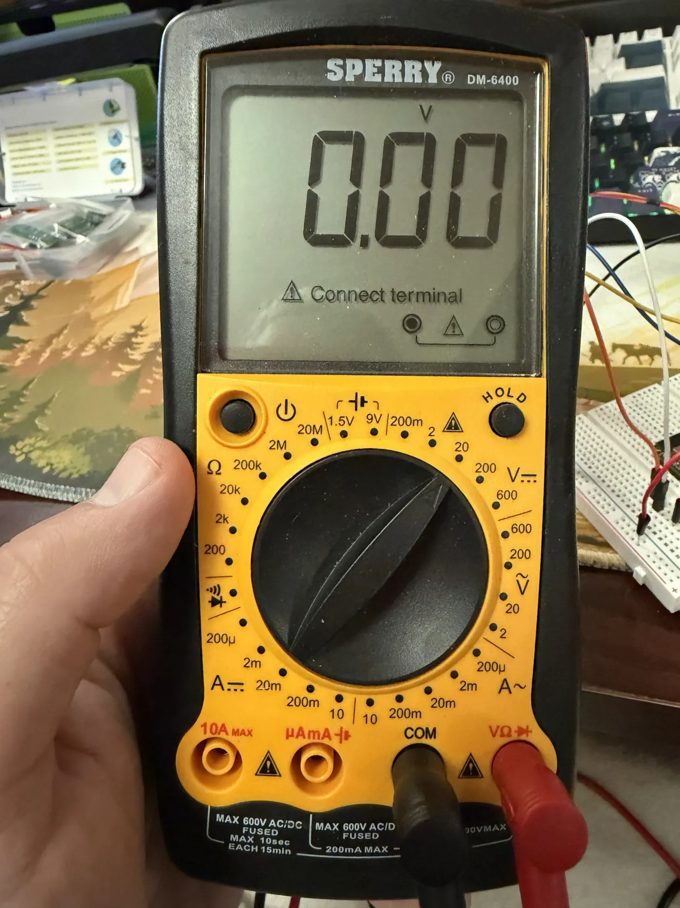 Sperry DM-6400 multimeter reading 0.00V, held over the breadboard