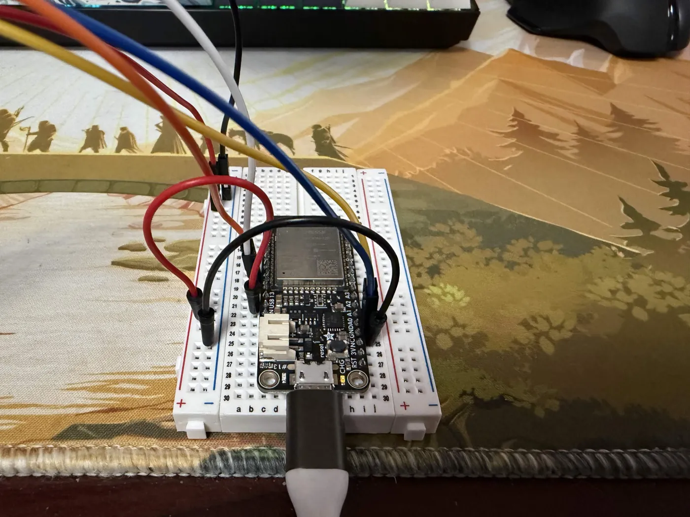 Close-up of the Adafruit HUZZAH32 on a breadboard showing tiny GPIO pin silkscreen labels along the board edge