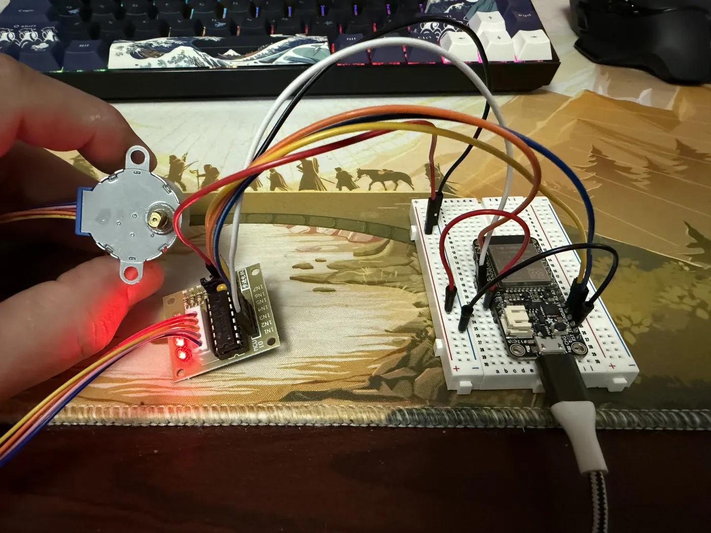 28BYJ-48 stepper motor held up next to the ULN2003 driver board with signal LEDs lit red, connected via jumper wires to the ESP32 breadboard