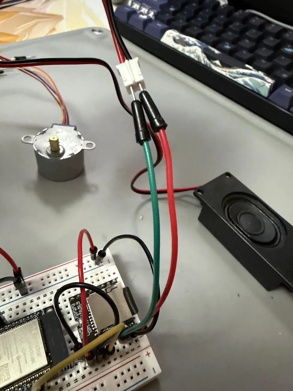 Full system laid out on the bench: stepper motor, breadboard with ESP32, and speaker connected end to end