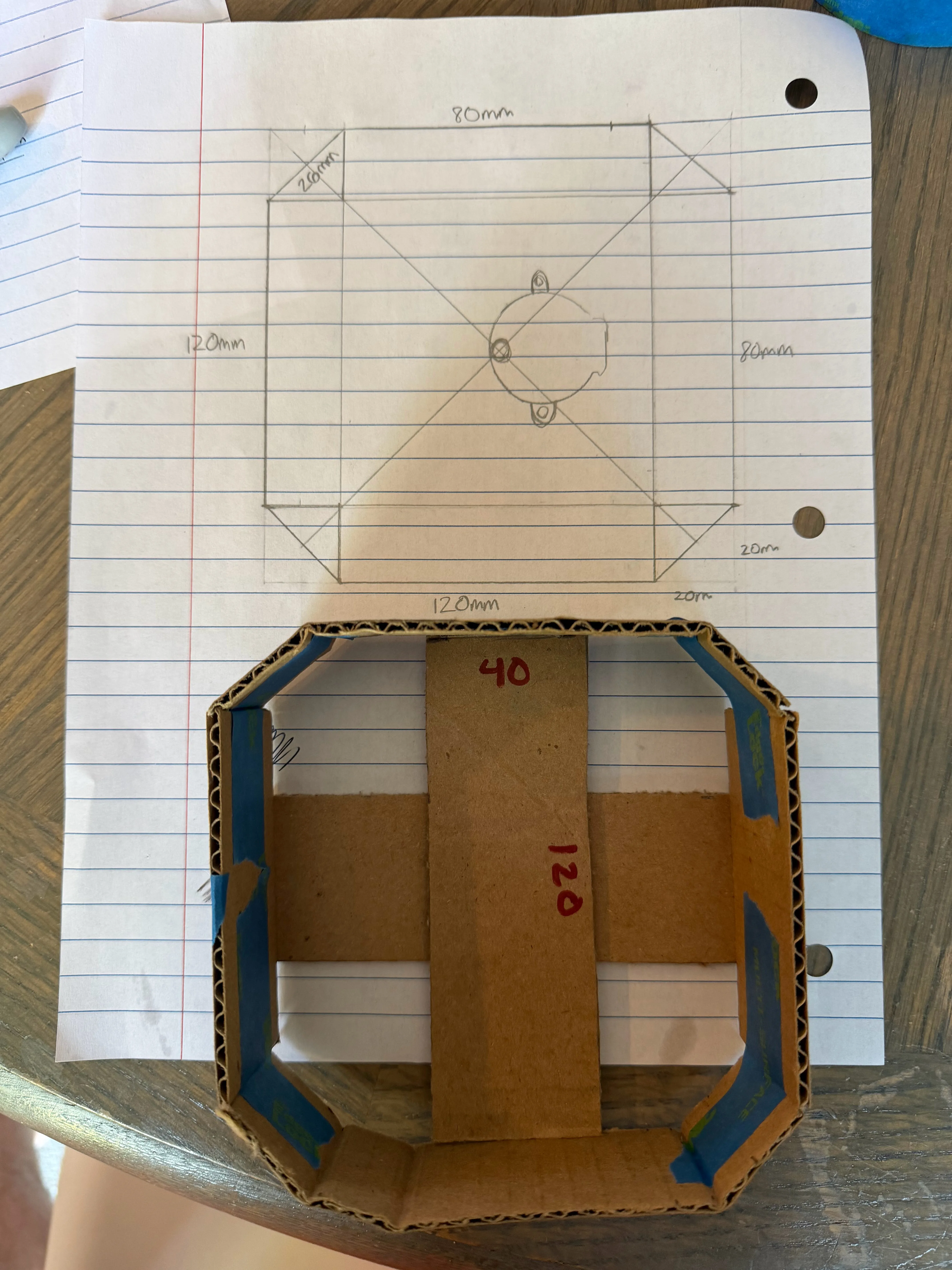 Assembled cardboard mockup of the octagonal housing sitting directly on top of the pencil footprint sketch, dimensions matching