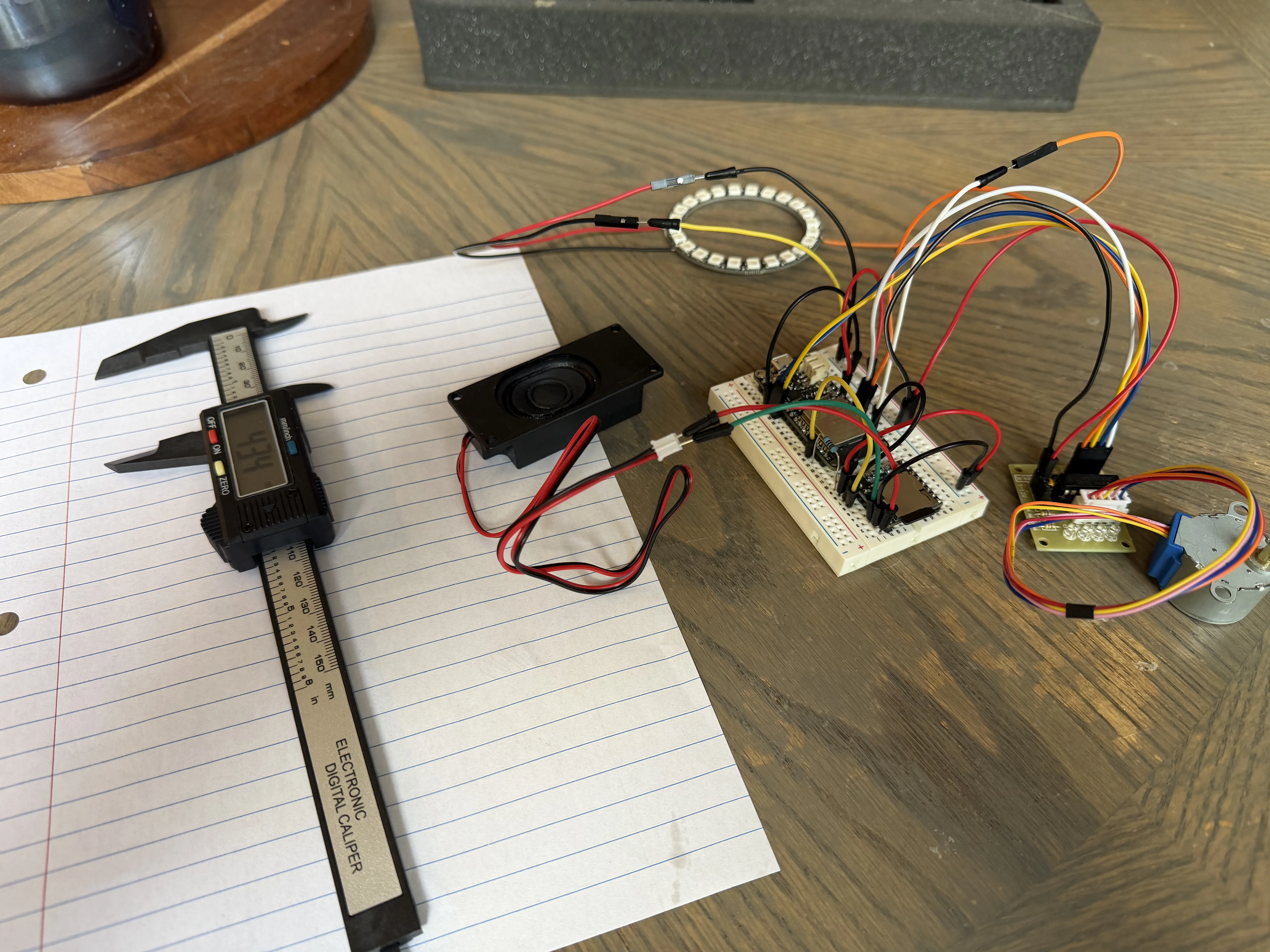 Complete electronics stack wired on a breadboard: ESP32, NeoPixel ring, stepper driver and motor, DFPlayer, and speaker, sitting next to a foam tool case