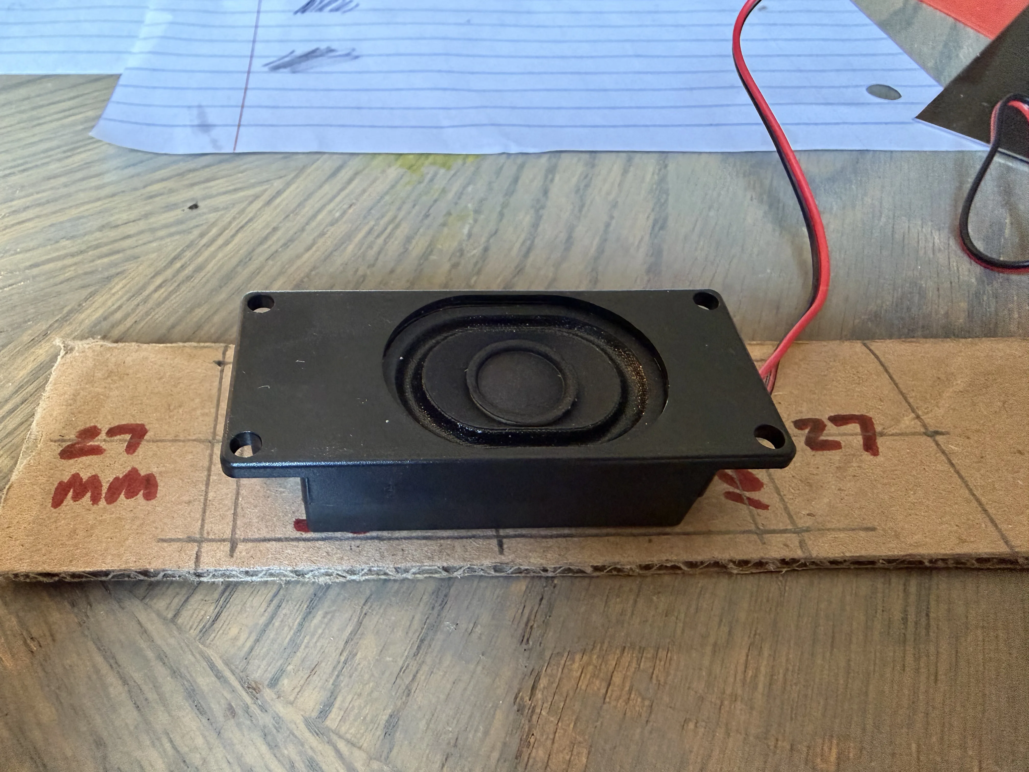 The speaker component test-fitted against cutout marks drawn in red marker on a cardboard strip