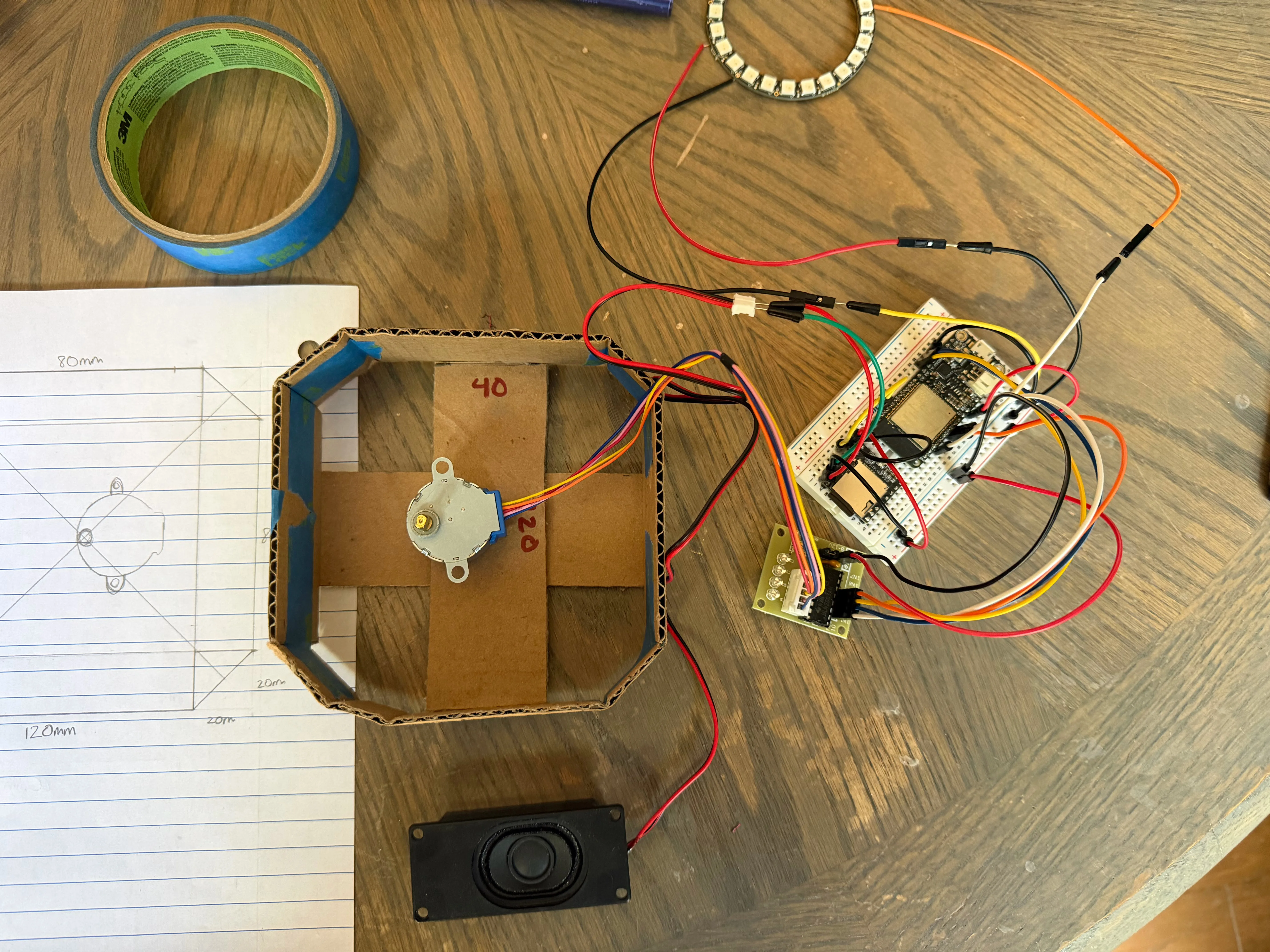 Stepper motor mounted on the cardboard cross-brace inside the mockup housing, with the breadboard electronics staged alongside